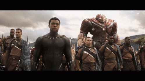 A Man In A Black Suit Stands In A Line With Other Men GIF