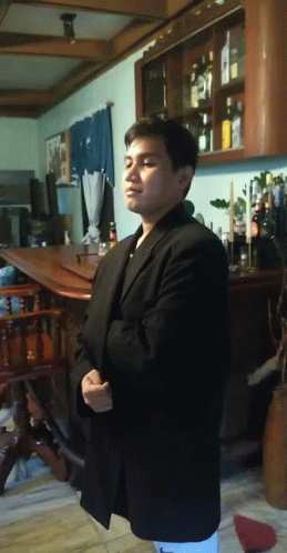 a man in a black suit stands in front of a shelf full of bottles