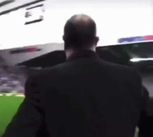A Man In A Black Suit Stands In Front Of A Stadium GIF