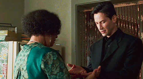 A Man In A Black Suit Stands Next To A Woman In A Green Dress GIF