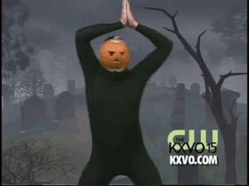 A Man In A Black Suit With A Pumpkin On His Head Is Dancing In A Cemetery . GIF