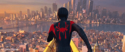 A Man In A Black Suit With A Red Spider On His Back Stands In Front Of A City Skyline GIF