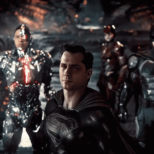 A Man In A Black Superman Costume Is Standing In Front Of A Group Of Robots GIF