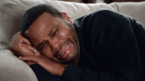 A Man In A Black Sweater Is Laying On A Couch Crying . GIF