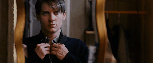 A Man In A Black Sweater Is Looking At Himself In A Mirror GIF