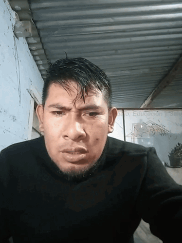 A Man In A Black Sweater Is Looking At The Camera With A Sign In The Background That Says Dr. Eduardo Garcia GIF