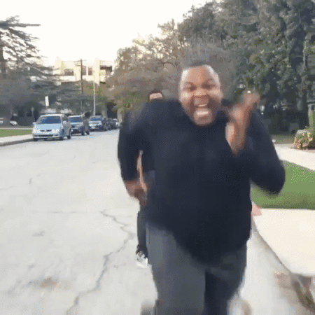 A Man In A Black Sweater Is Running Down A Street And Making A Funny Face GIF