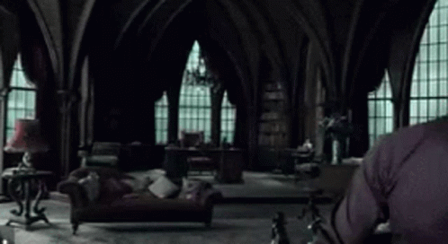 A Man In A Black Sweater Is Sitting In A Living Room With A Couch And A Lamp . GIF