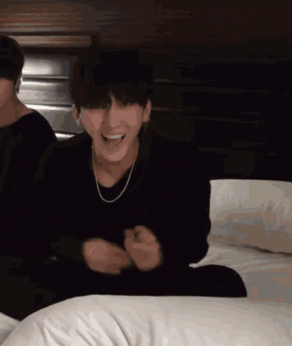 A Man In A Black Sweater Is Sitting On A Bed GIF