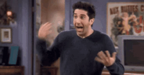 A Man In A Black Sweater Is Standing In A Living Room With His Mouth Open And His Hands Outstretched . GIF
