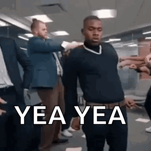 A Man In A Black Sweater Is Standing In A Room With A Group Of People And Says Yea Yea . GIF