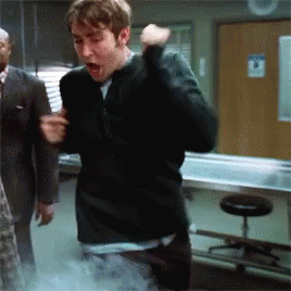 a man in a black sweater is standing in a room with a sign on the wall that says no smoking