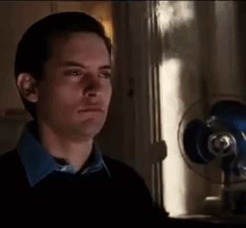 A Man In A Black Sweater Is Standing In Front Of A Fan . GIF