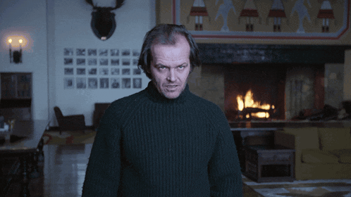a man in a black sweater is standing in front of a fireplace