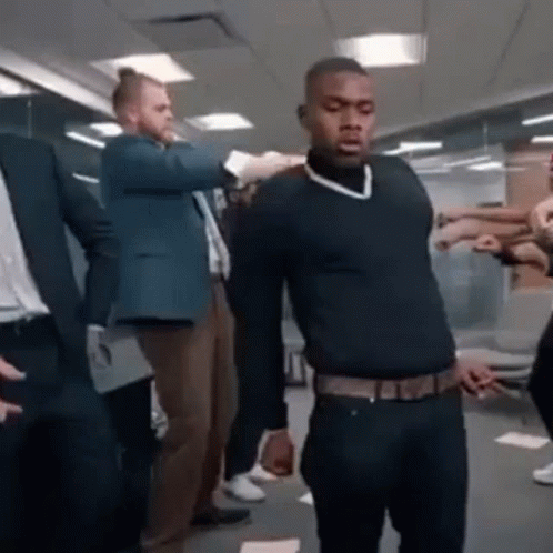 A Man In A Black Sweater Is Standing In Front Of A Group Of People In A Room . GIF