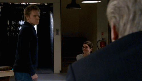 a man in a black sweater stands in front of a fire extinguisher in a dark room