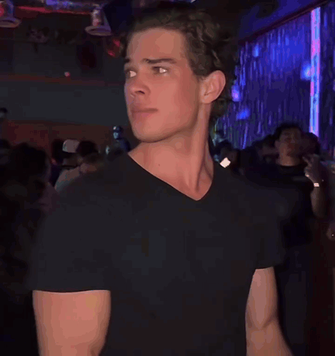 a man in a black t-shirt is standing in a crowded room