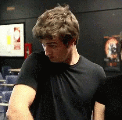 A Man In A Black T-Shirt Is Standing In A Dark Room . GIF