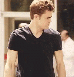 A Man In A Black T-Shirt Is Standing In Front Of A Door GIF