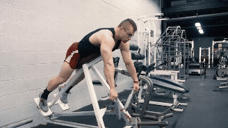 A Man In A Black Tank Top And Red Shorts Is Using A Machine In A Gym GIF