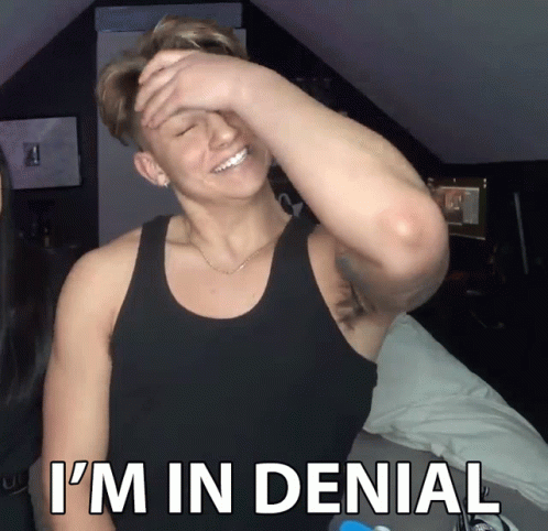 A Man In A Black Tank Top Covering His Face With His Hand And The Words I 'M In Denial Below Him GIF