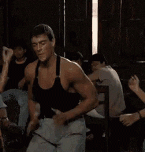 A Man In A Black Tank Top Is Dancing In A Room With Other People GIF