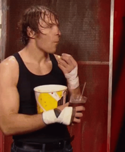 A Man In A Black Tank Top Is Holding A Cup Of Popcorn And A Drink . GIF
