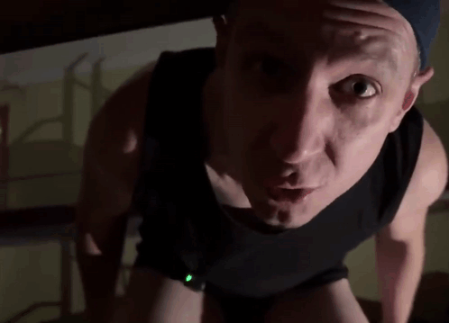 A Man In A Black Tank Top Is Looking At The Camera With His Mouth Open . GIF