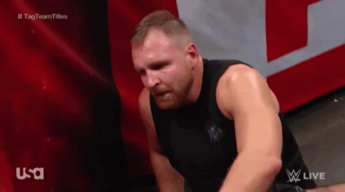 A Man In A Black Tank Top Is Sitting On The Floor With His Head Down . GIF