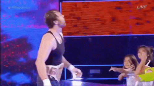 A Man In A Black Tank Top Is Standing In A Wrestling Ring With A Group Of Children . GIF