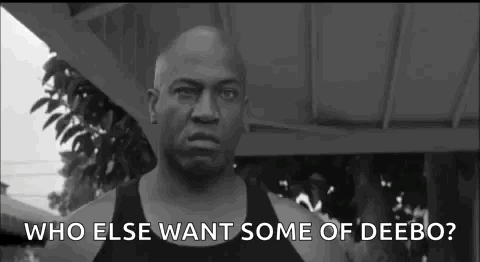 A Man In A Black Tank Top Is Standing In Front Of A Building And Asking Who Else Wants Some Of Deebo . GIF