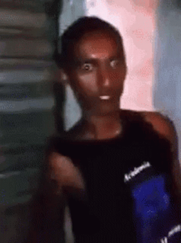 A Man In A Black Tank Top Is Standing In Front Of A Building . GIF