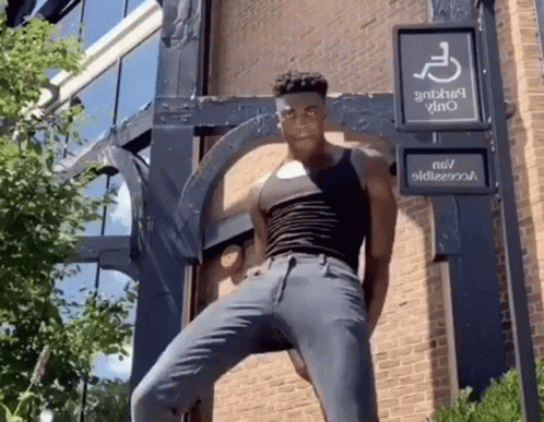 A Man In A Black Tank Top Is Standing In Front Of A Handicap Sign GIF