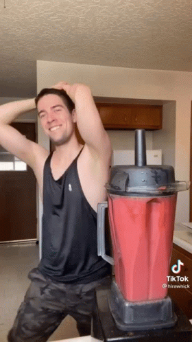 A Man In A Black Tank Top Is Standing Next To A Red Blender GIF