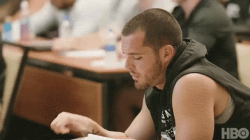 A Man In A Black Tank Top Sits At A Table With A Hbo Logo On The Bottom GIF