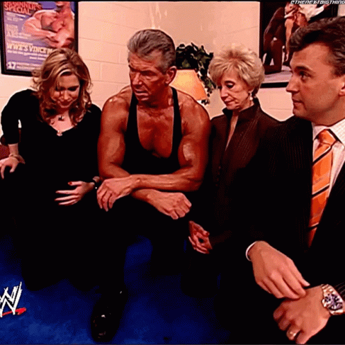 A Man In A Black Tank Top Sits Between Two Women And A Man In An Orange Tie GIF