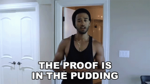 A Man In A Black Tank Top Stands In Front Of A Door With The Words The Proof Is In The Pudding Above Him GIF