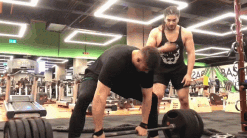 A Man In A Black Tank Top With A Skull On It Is Helping Another Man Lift A Barbell GIF