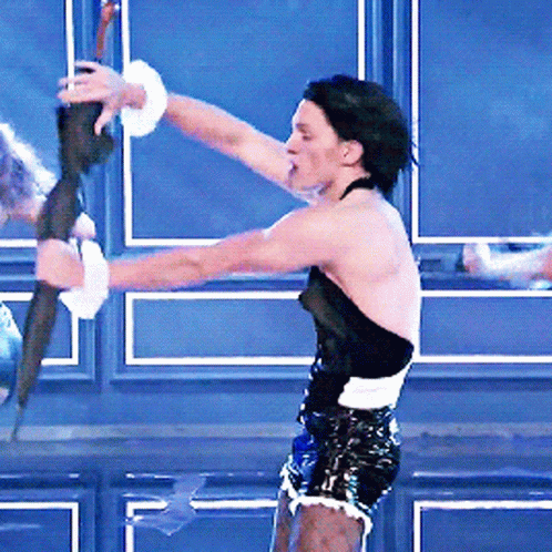 A Man In A Black Top And Shorts Is Holding A Stick GIF