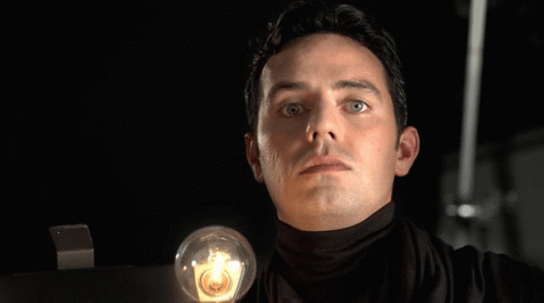 A Man In A Black Turtleneck Is Holding A Light Bulb In Front Of The Word Thats GIF