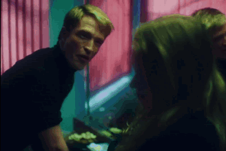 A Man In A Black Turtleneck Talks To A Woman In A Dark Room GIF