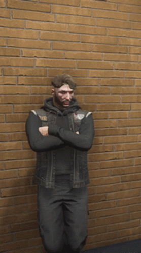 A Man In A Black Vest Is Standing In Front Of A Brick Wall GIF