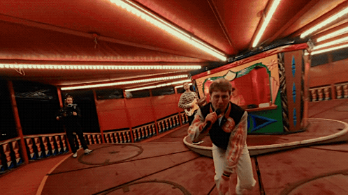 A Man In A Bloody Vest Is Holding A Microphone In A Room GIF
