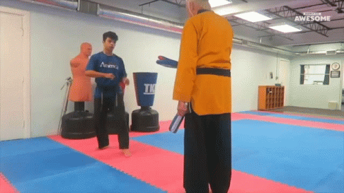 A Man In A Blue Academy Shirt Is Kicking A Man In A Yellow Robe GIF
