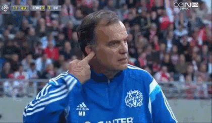 A Man In A Blue Adidas Jacket Is Covering His Ears During A Soccer Game GIF