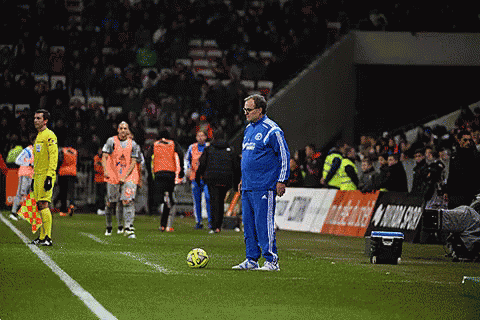 A Man In A Blue Adidas Jacket Stands Next To A Soccer Ball On A Field GIF