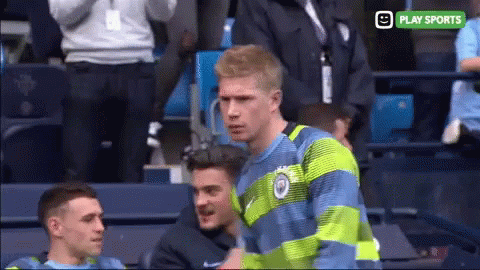 A Man In A Blue And Green Striped Shirt Stands In A Stadium With A Play Sports Logo Behind Him GIF