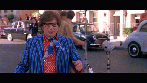 A Man In A Blue And Red Striped Suit And Tie Stands On A Street GIF