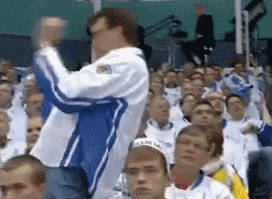 A Man In A Blue And White Jacket Is Standing In Front Of A Crowd Of People GIF