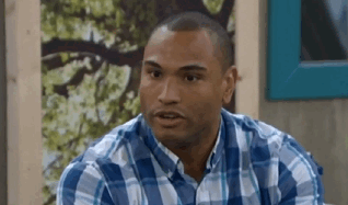 A Man In A Blue And White Plaid Shirt Is Sitting In Front Of A Wall . GIF